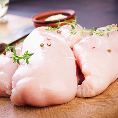 Raw chicken breast fillets on wooden cutting board with herbs and spices.